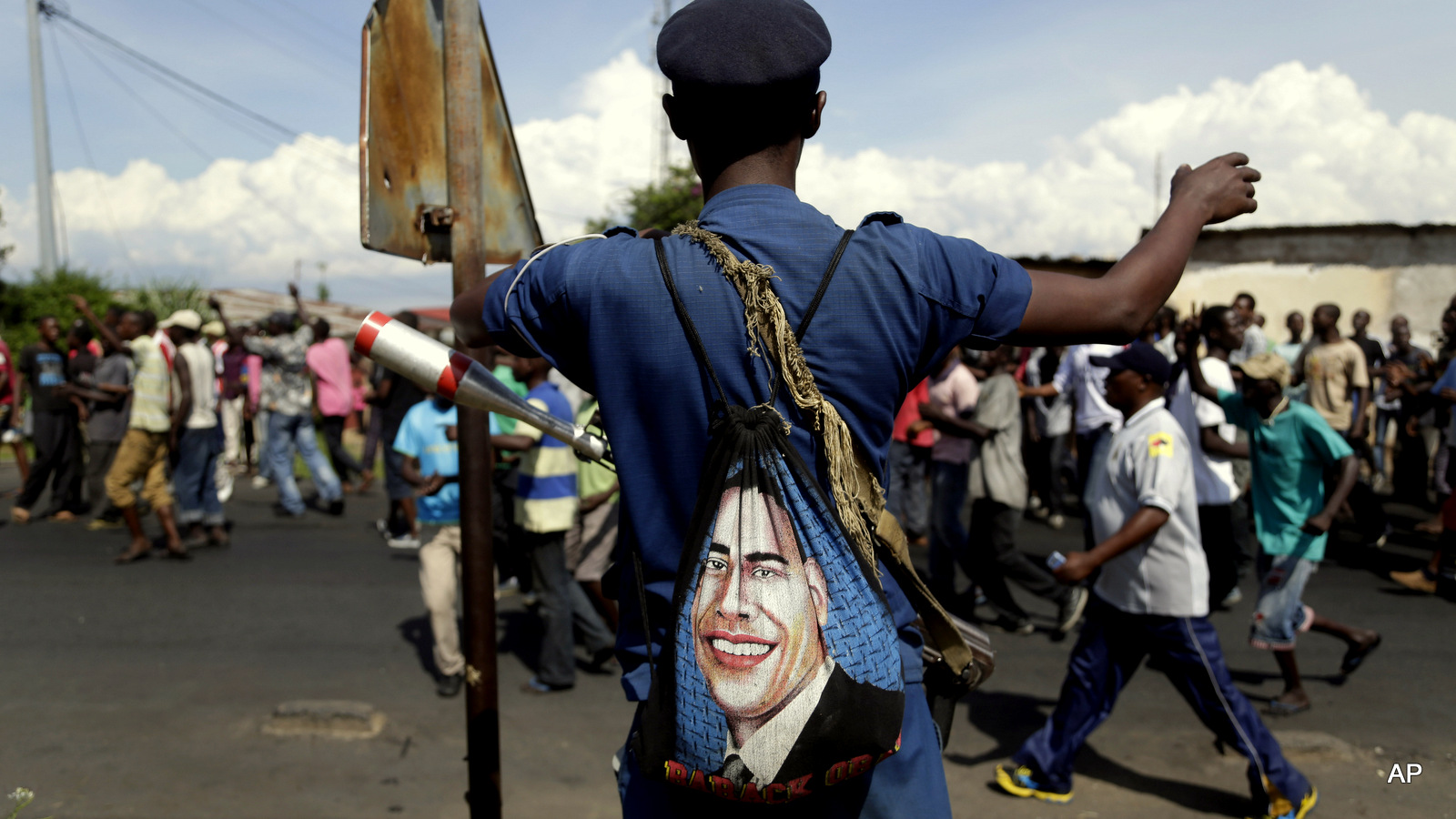 A police officer with a bag depicted the image of US President Barack Obama, stands on patrol as protesters march through the Musaga district of Bujumbura, in Burundi, Monday, May 11, 2015. Police and army negotiated with over 2000 protesters to allow delivery trucks to enter the city. One person was killed in a clash with Burundi's police on Sunday in demonstrations in the capital, Bujumbura, as the government ordered a ban on any further street protests over President Pierre Nkurunziza's bid for a third term in power.
