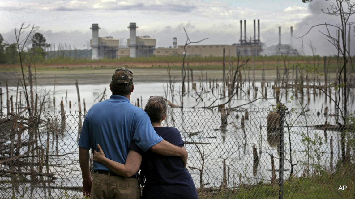 Bryant Gobble, left, hugs his wife, Sherry Gobble, right, as they look from their yard across an ash pond full of dead trees toward Duke Energy's Buck Steam Station in Dukeville, N.C. Records obtained by The Associated Press show that Duke and North Carolina environmental regulators have known since 2011 that groundwater samples taken from monitoring wells near several homes in Dukeville contained substances, some that can be toxic, exceeding state standards.