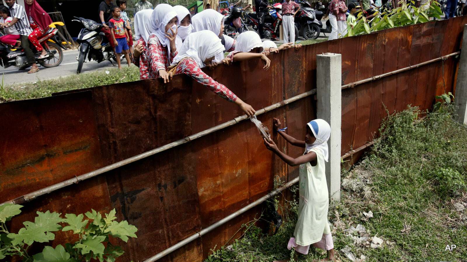 School children hand out food to a Rohingya young girl from outside the fence of a temporary shelter in Bayeun, Aceh province, Indonesia, Thursday, May 21, 2015. In the past three weeks, thousands of people — Rohingya Muslims fleeing persecution in Myanmar and Bangladeshis trying to escape poverty — have landed in overcrowded boats on the shores of Indonesia, Malaysia and Thailand. After initially pushing many boats back, Malaysia and Indonesia announced on Wednesday that they will offer temporary shelter to all incoming migrants.