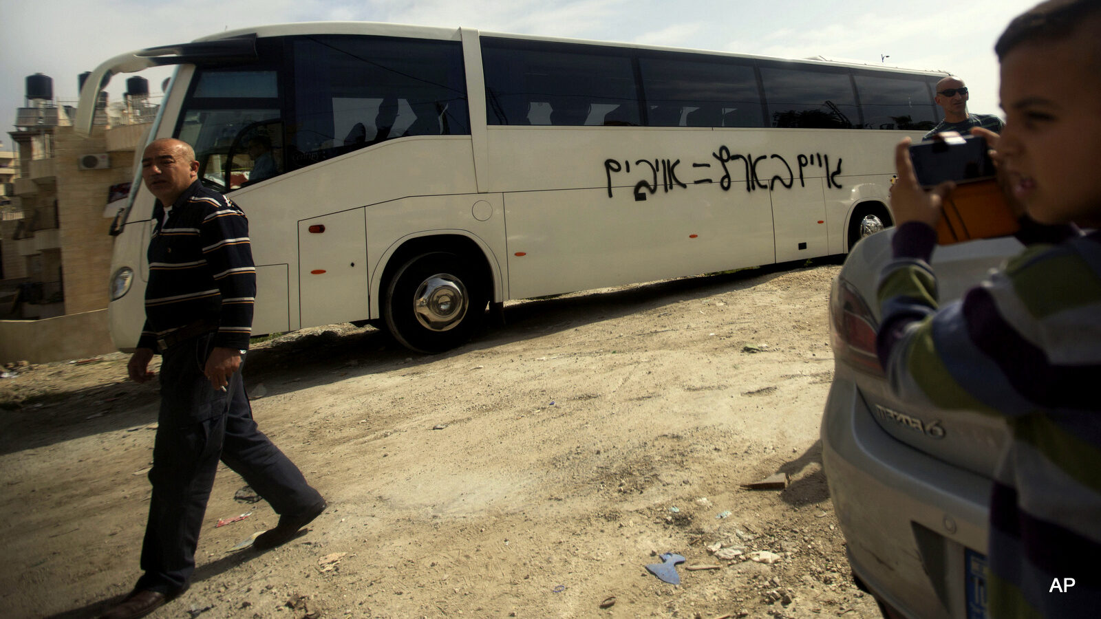 A Palestinian boy takes a photo of graffiti with Hebrew that reads "non-Jews in Israel equals enemies," on a bus in an Arab neighborhood in Jerusalem, Monday, March 24, 2014. Israeli police say vandals have slashed car tires and sprayed a bus with hate graffiti in a predominantly Arab neighborhood in Jerusalem.