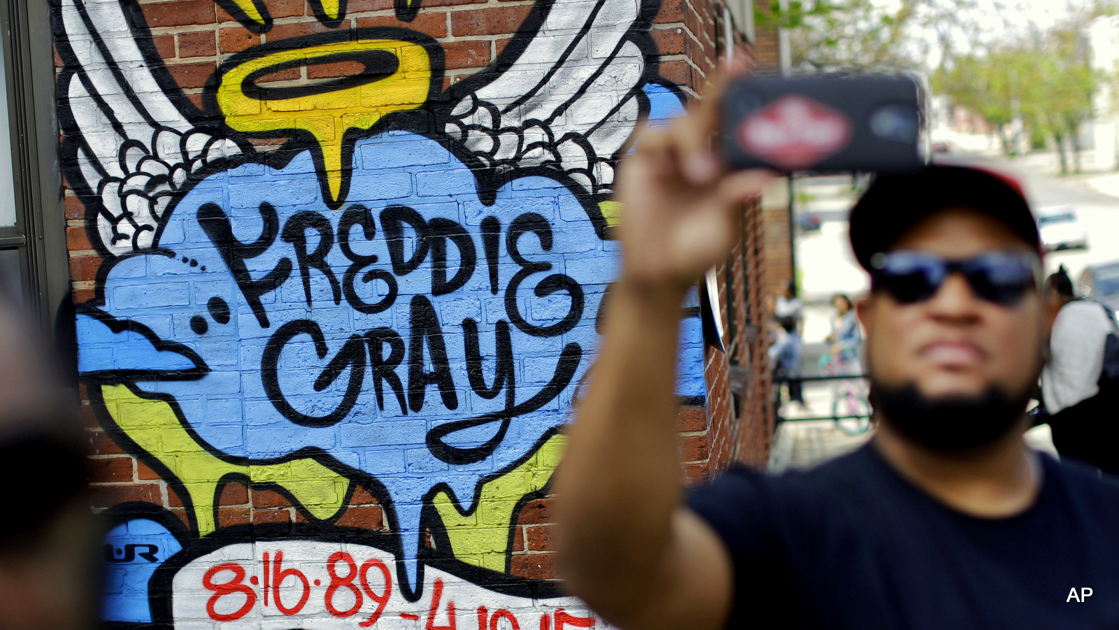 J.R. White, right, takes a selfie in front of a mural that was painted at the site of Freddie Gray's arrest, Saturday, May 2, 2015, in Baltimore, as protesters prepare to march to City Hall.  Six police officers were charged Friday with felonies ranging from assault to murder in Gray's death. In announcing the charges, State's Attorney Marilyn Mosby said police had no reason to stop or chase Gray in the first place when they confronted him on April 12. He died of injuries on April 19. (AP Photo/Patrick Semansky)