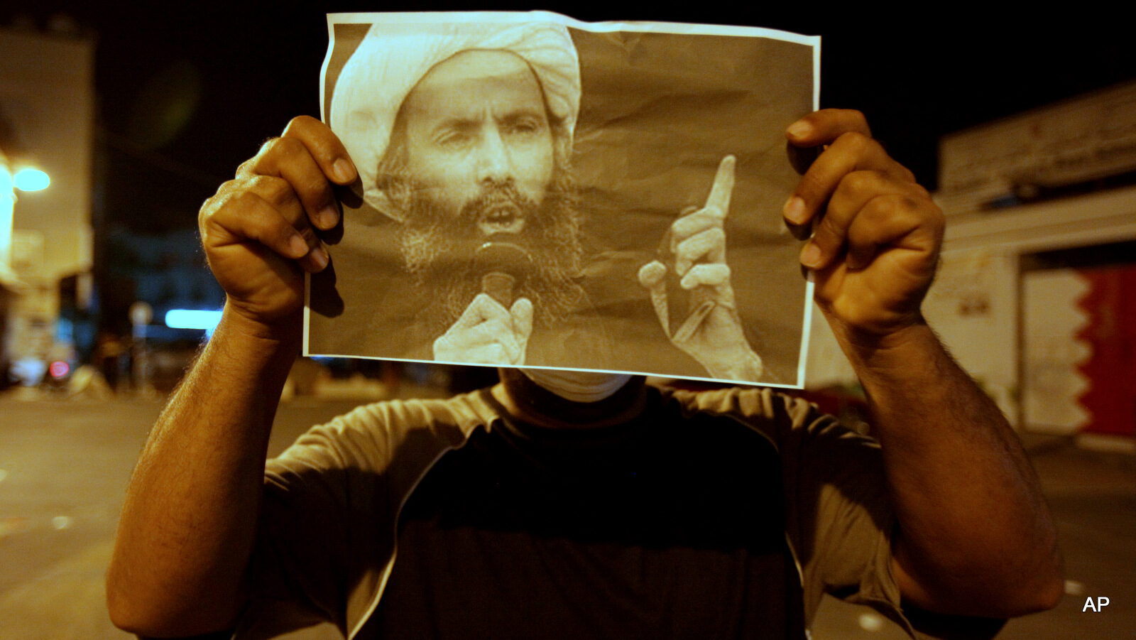 A Bahraini anti-government protester holds up a picture of jailed Saudi Sheik Nimr al-Nimr during clashes with riot police in Sanabis, Bahrain, a suburb of the capital Manama, Wednesday night, Oct. 15, 2014. The outspoken and widely revered Shiite cleric was convicted Wednesday in Saudi Arabia of sedition and other charges and sentenced to death, raising fears of renewed unrest from his supporters in the kingdom and neighboring Bahrain.