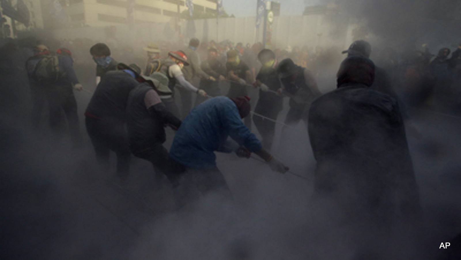 Members of the Korean Confederation of Trade Unions try to move a bus blocking a street by pulling ropes they tied near the police vehicle's wheels as police spray fire extinguisher on them after their May Day rally against the government labor policy and the handling of a ferry disaster that killed more than 300 people a year ago in Seoul, South Korea, Friday, May 1, 2015. Demonstrators occupied several downtown streets and sporadically clashed with police officers, who created tight perimeters with their buses to block the marchers. There were no immediate reports of injuries. 