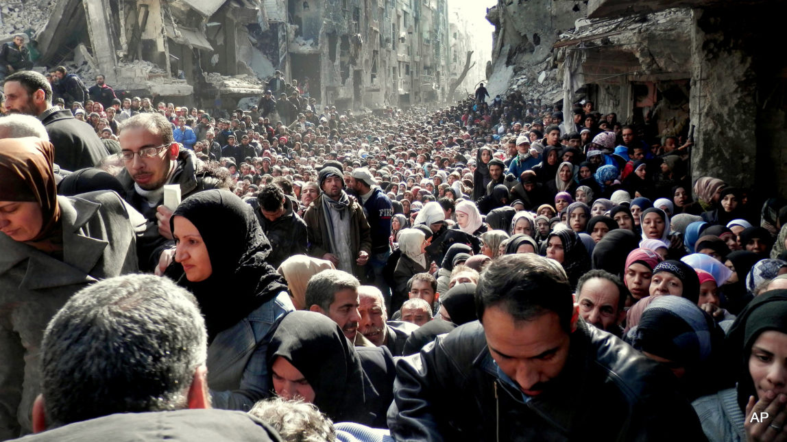 This picture taken on Jan. 31, 2014, and released by the United Nations Relief and Works Agency for Palestine Refugees (UNRWA), shows residents of the besieged Palestinian camp of Yarmouk, queuing to receive food supplies, in Damascus, Syria. A Norwegian humanitarian group report says a record 38 million people have been internally displaced in their countries worldwide, with 2.2 million Iraqis alone fleeing in 2014 after ISIS seized their areas. (UNRWA via AP, File)