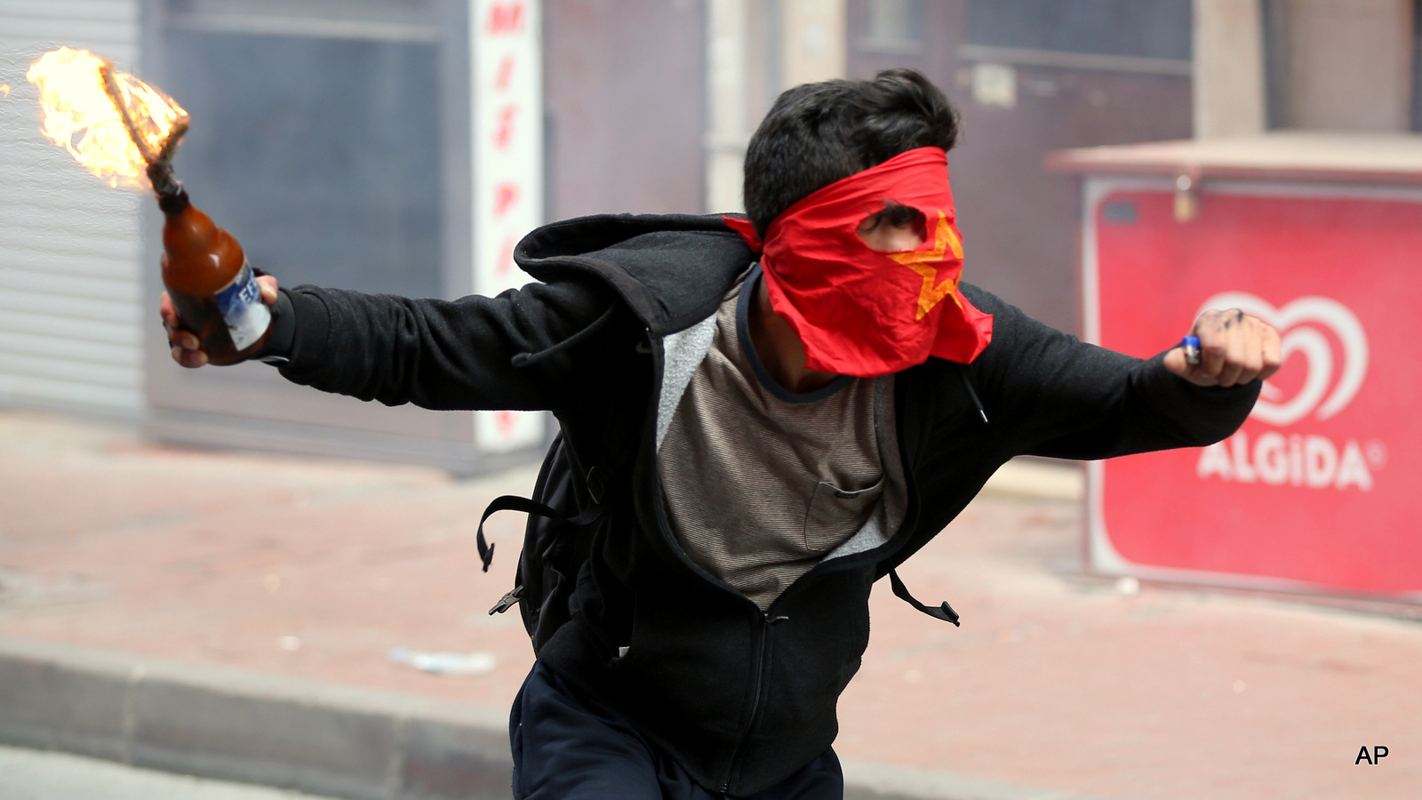 A demonstrator runs to hurl a firebomb towards riot police officers during clashes in Istanbul, Turkey, Friday, May 1, 2015.  Clashes erupted between police and May Day demonstrators in Istanbul on Friday as crowds determined to defy a government ban tried to march to the city's iconic Taksim Square.  Security forces pushed back demonstrators with a water cannon and tear gas. 