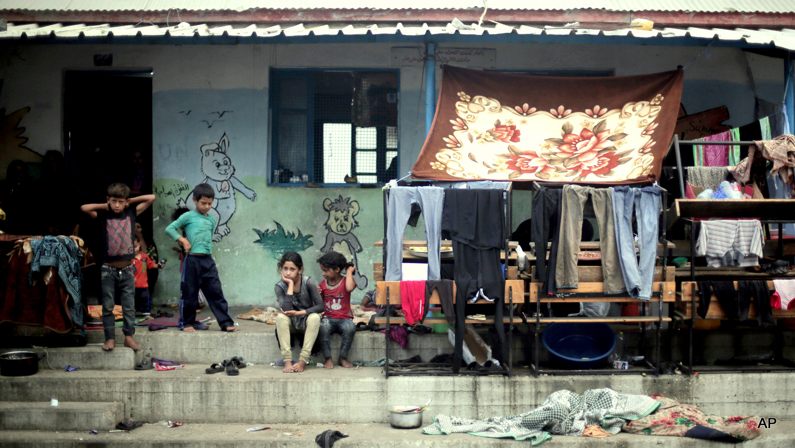 Palestinian children sit next to hanged clothes, on the First day of Eid al-Fitr in a United Nations school where dozens of families have sought refuge after fleeing their homes in fear of Israeli airstrikes, in the Jabaliya refugee camp, northern Gaza Strip. A U.N. inquiry has found that at least 44 Palestinians were killed and at least 227 injured by "Israeli actions" while sheltering at U.N. locations during last year's Gaza war. Secretary Ban Ki-moon said Monday, April 27, 2015, he deplores the deaths and calls U.N. locations "inviolable."