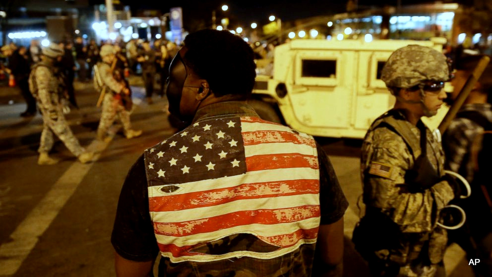 A protester watches soldiers pass as curfew approaches, Friday, May 1, 2015, in Baltimore.