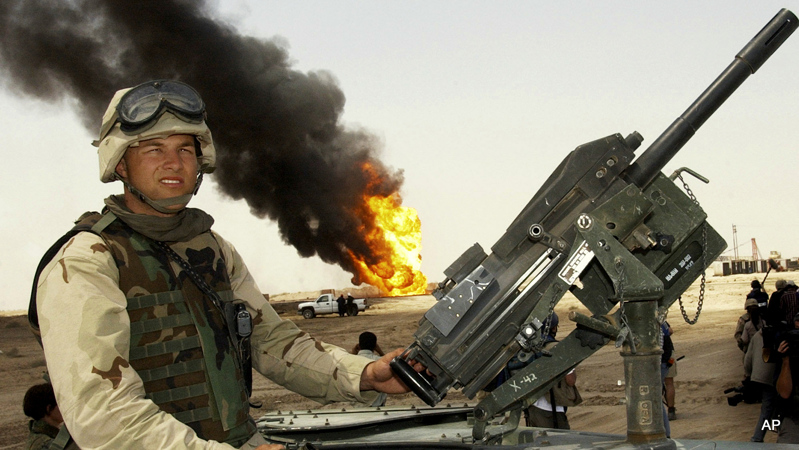 En esta foto de archivo del 1 de abril de 2003, un soldado de los EE. UU. Hace guardia sobre un humvee mientras los trabajadores petroleros trabajan en incendios de pozos petroleros en el campo petrolero Rumaila, en el sur de Irak.