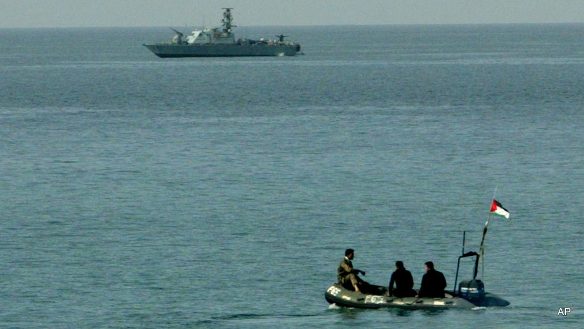 Palestinian police officers sit in a small boat as they pass near an Israeli naval vessel