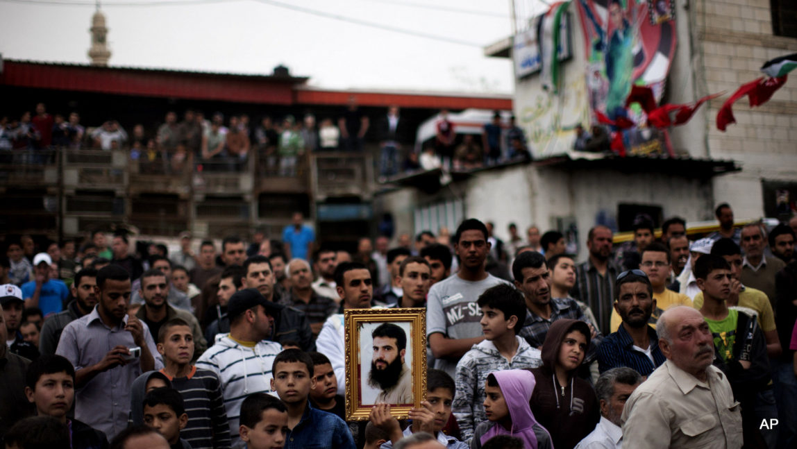 A Palestinian holds a picture of a Palestinan prisoner jailed in Israel during a celebration for the liberation of Palestinian Khader Adnan in the West Bank village of Arrabeh, near Jenin, Wednesday, April 18, 2012.