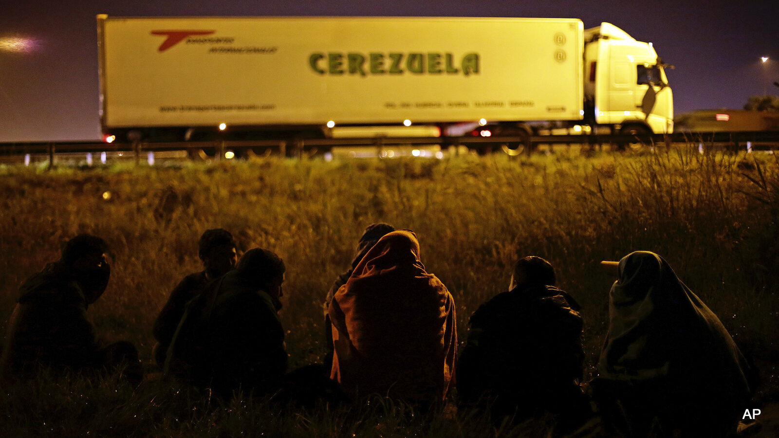 Migrants wait along a motorway leading to a ferry port to cross the English Channel, in Calais, northern France,