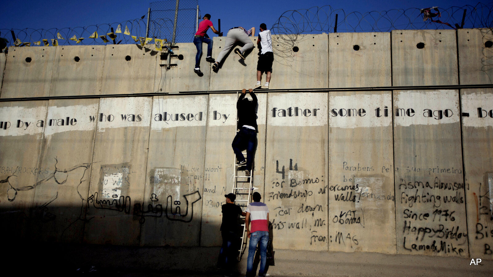 Young Palestinians use a ladder to climb over the Israeli apartheid wall