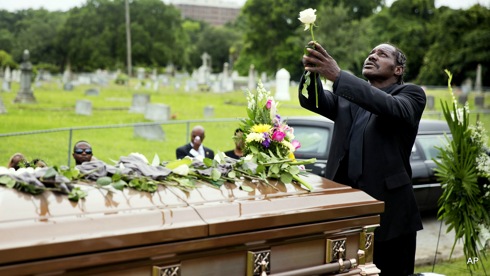 Gary Washington holds up a rose before placing it on the casket of his mother, Ethel Lance, following her burial service