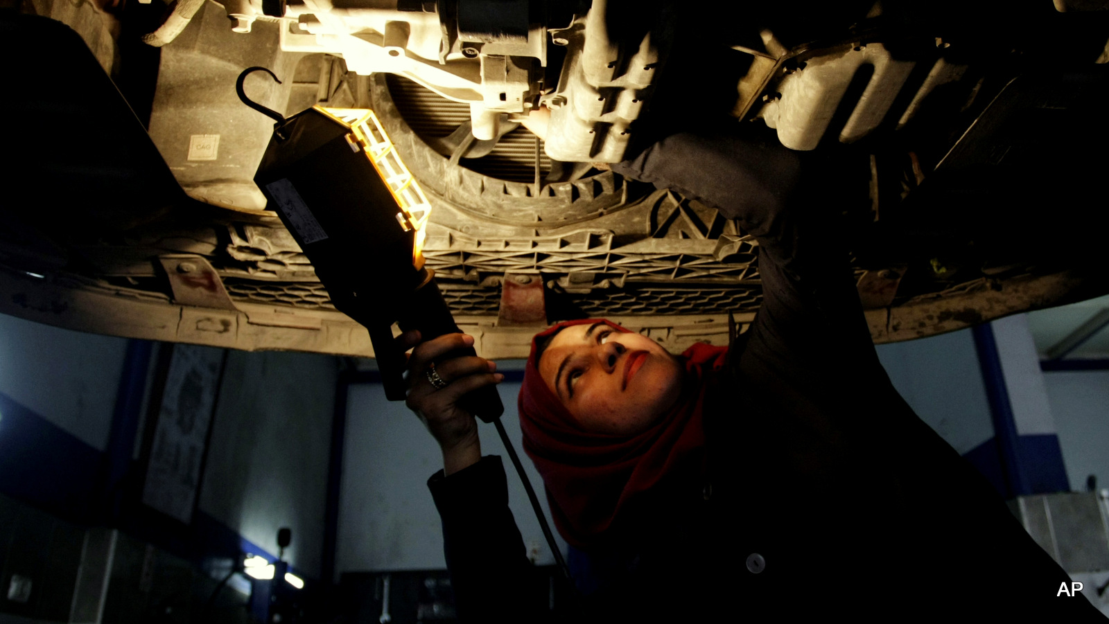 Palestinian auto mechanic Nagham Dweikat checks the bottom of a vehicle at a repair shop