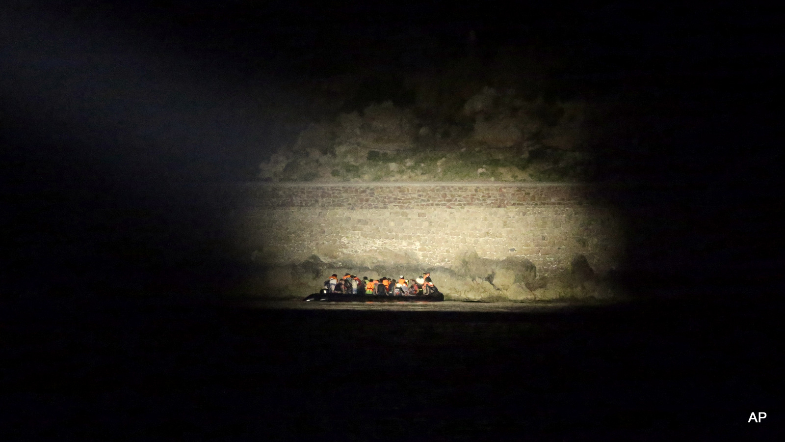 A Greek coast guard vessel uses a light to spot migrants arrive on an overcrowded dinghy from Turkish coasts