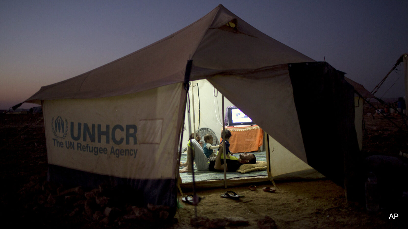 A Syrian refugee seen through the doorway of his tent plays with his children at an informal tented settlement