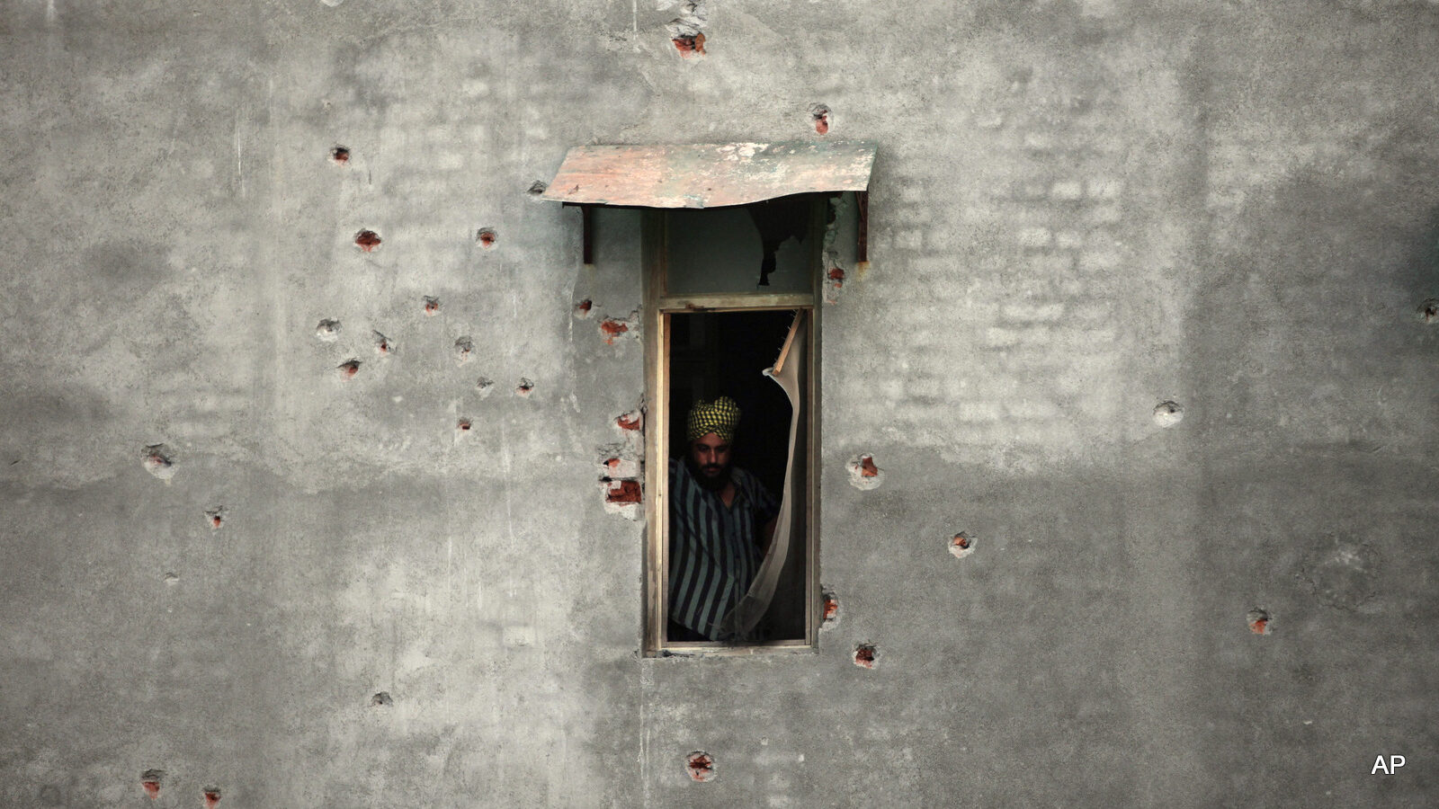 A civilian is seen through the window of a residential building, the walls of which have bullet marks following a rebel attack in the town of Dinanagar, in the northern state of Punjab, India, Monday, July 27, 2015. Indian forces fought an extended gunbattle Monday with militants who attacked a moving bus and stormed into a police station in a northern town bordering Pakistan.