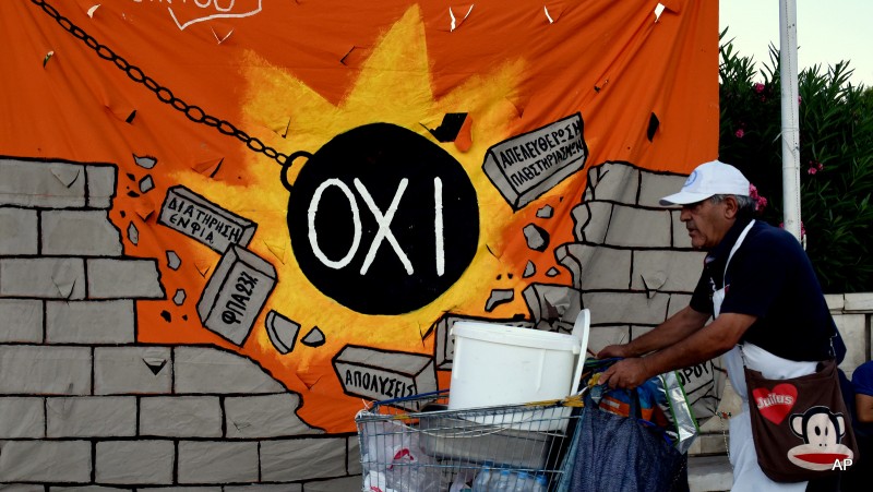 A street vendor pushes his trolley as he passes a banner, depicting a wrecking ball that reads: "NO" and destroying a wall with anti-austerity measures, in Athens, Wednesday, July 22, 2015. Barely a week after their last crunch vote, Greek lawmakers are set to vote later Wednesday on further economic reforms demanded by international creditors in return for a new financial bailout.