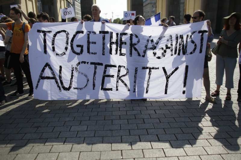 Demonstrators hold a poster against the austerity policy of Germany prior to a special session of the parliament Bundestag on negotiations with Greece for a new bailout in Berlin, Germany, Friday, July 17, 2015. (AP Photo/Markus Schreiber)
