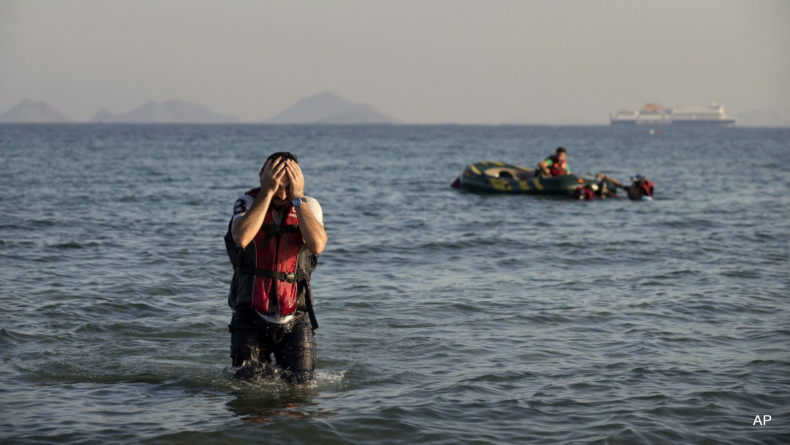 A Syrian Refugee arrives after crossing from Turkey by a rubber boat, seen in the background, in the southeastern island of Kos, Greece