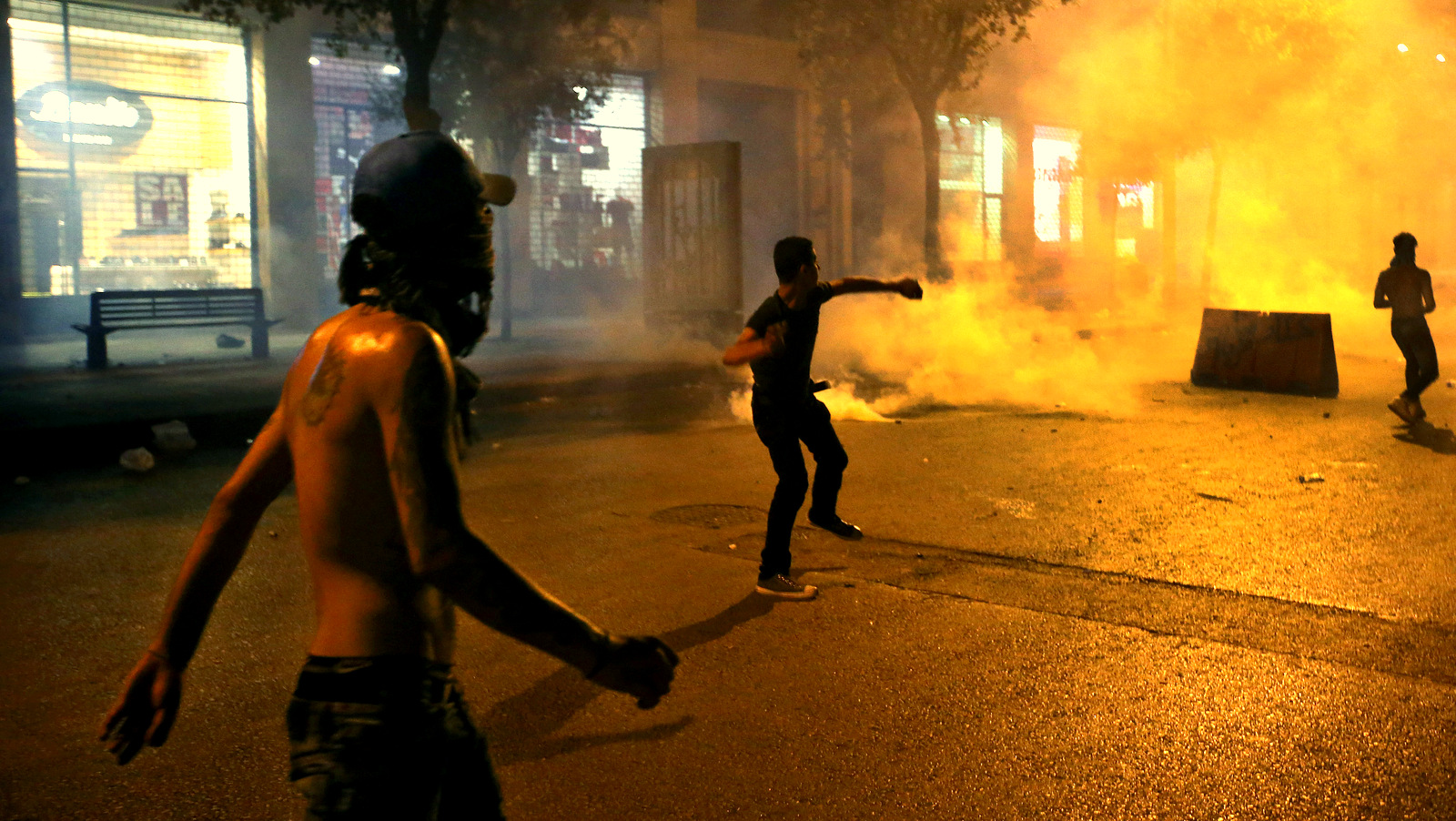 Lebanese anti-government protesters throw stones against the riot policemen, not seen, as smoke rise from the tear gas canisters, during a protest against an ongoing trash crisis, in downtown Beirut, Lebanon, late Sunday, Aug. 23, 2015. Lebanese riot police battled in the streets of downtown Beirut for a second night Sunday after demonstrators rallied over government corruption and an ongoing trash crisis. (AP Photo/Hussein Malla)