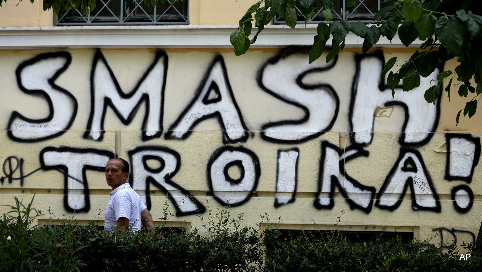A pedestrian passes graffiti referring to the officials from the European Union, European Central Bank and International Monetary Fund, together known as the troika, in Athens, Wednesday, July 29, 2015.