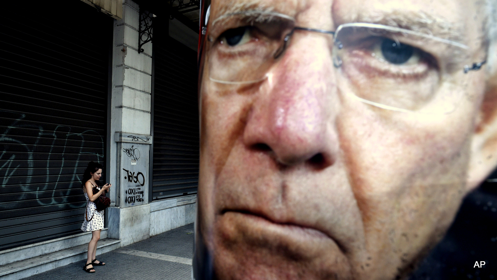 A woman uses her cell phone next to a poster depicting German Finance Minister Wolfgang Schaeuble placed by supporters of the No vote to the referendum in the northern Greek port city of Thessaloniki, Friday, July 3, 2015.