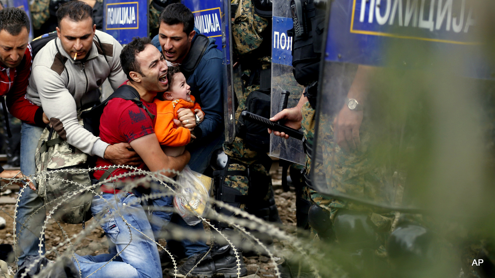 Migrant men help a fellow migrant man holding a boy as they are stuck between Macedonian riot police officers and migrants during a clash near the border train station of Idomeni, northern Greece, as they wait to be allowed by the Macedonian police to cross the border from Greece to Macedonia, Friday, Aug. 21, 2015. Macedonian special police forces have fired stun grenades to disperse thousands of migrants stuck on a no-man's land with Greece, a day after Macedonia declared a state of emergency on its borders to deal with a massive influx of migrants heading north to Europe. (AP Photo/Darko Vojinovic)