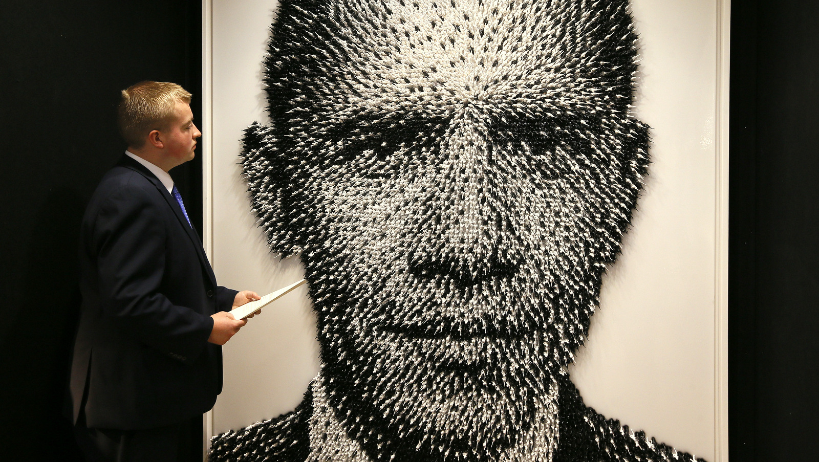 A Christie's employee looks at a portrait of Barack Obama by artist Joe Black called 'Shoot to Kill' made from thousands of plastic toy soldiers, during a press preview at Christie's auction rooms in London, Monday, Aug. 3, 2015. (AP Photo/Kirsty Wigglesworth)