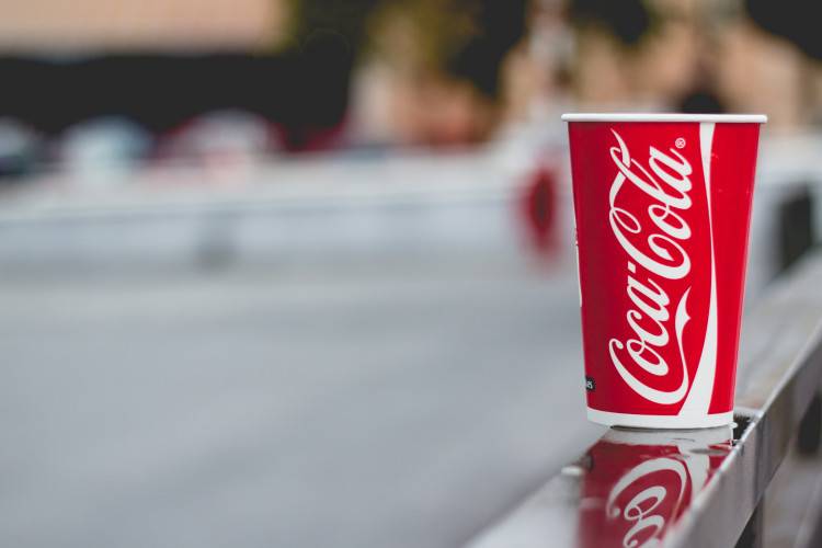 File: A paper cup branded with the Coca-Cola logo sits on a ledge. (Flickr / Leo Hidalgo)