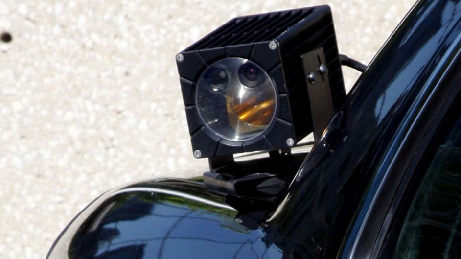 A camera mounted on the trunk of a police car scans traffic on the streets, aggregating data such as patterns on travel and frequency of visits to a certain area.