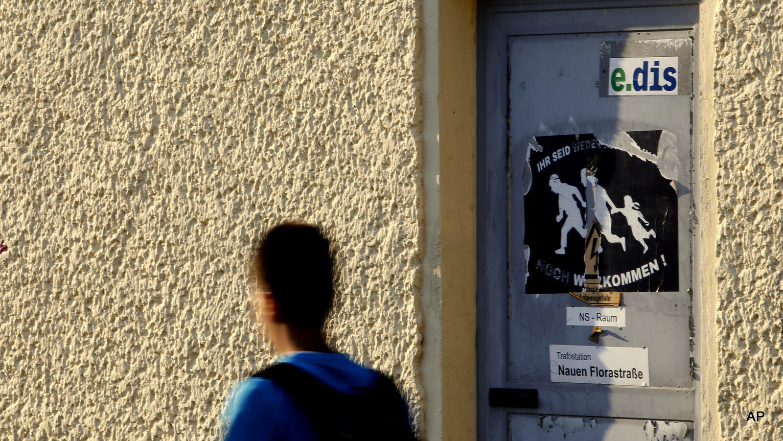 In Aug. 11, 2015 photo a boy walks past a torn poster "You are neither refugees nor are you welcome" in Nauen, eastern Germany. An initiative "Nein zum Heim" (No to the (refugee) home) protests against a planned shelter for asylum seekers. The starkly differing reactions to the influx of refugees points to an increasing polarization in Germany, with growing acceptance of outsiders by a majority but a persistent and possibly radicalized minority fearful of all things foreign.