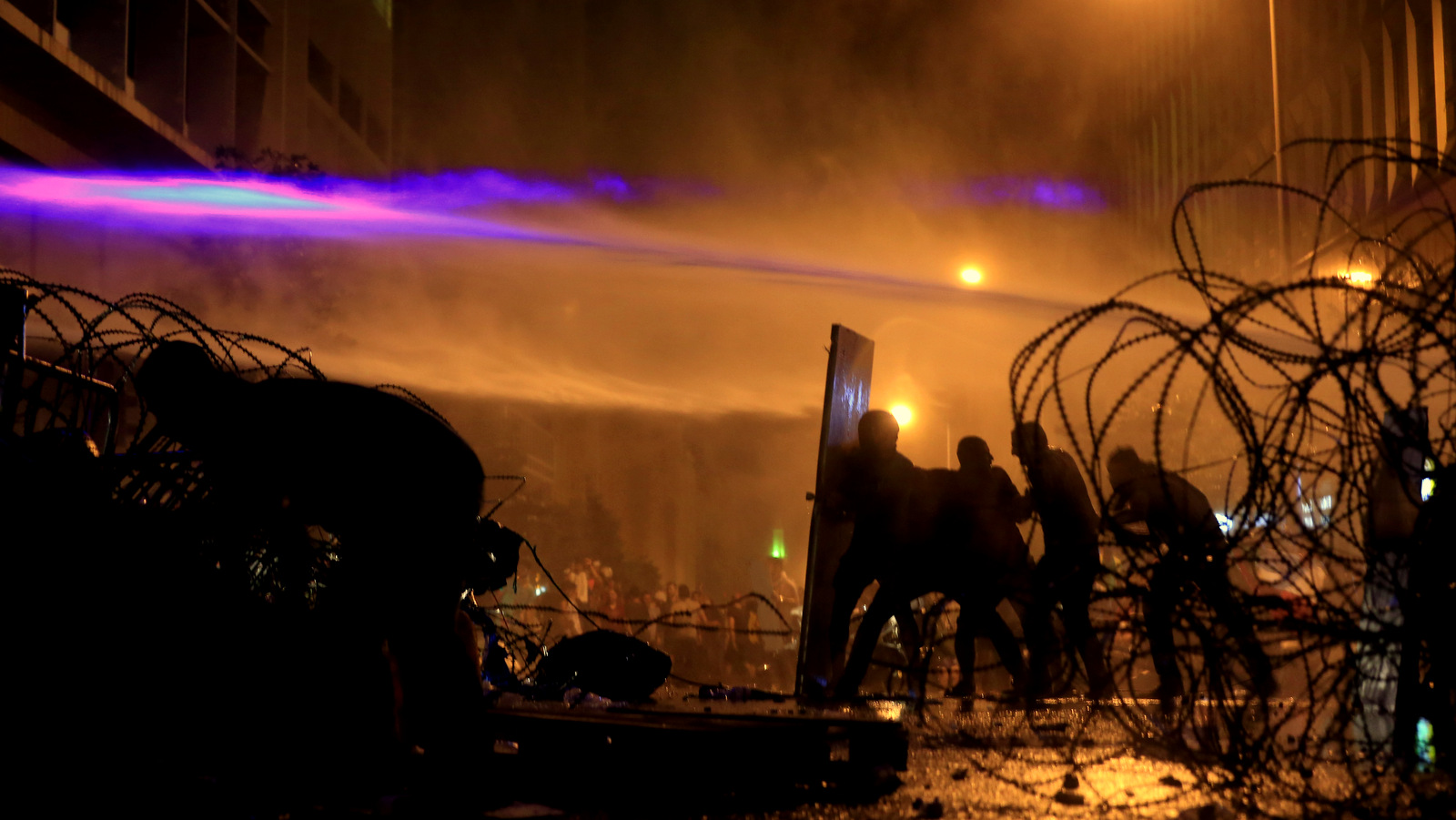 Lebanese activists hold up a makeshift shield, as they are sprayed by riot police using water cannons during a protest against the ongoing trash crisis, in downtown Beirut, Lebanon, Sunday, Aug. 23, 2015. Lebanese riot police fired several rounds of tear gas and water cannons for the second consecutive day in downtown Beirut Sunday as they battled protesters with batons and stones _ a marked escalation of mass demonstrations against an ongoing trash crisis. (AP Photo/Hassan Ammar)