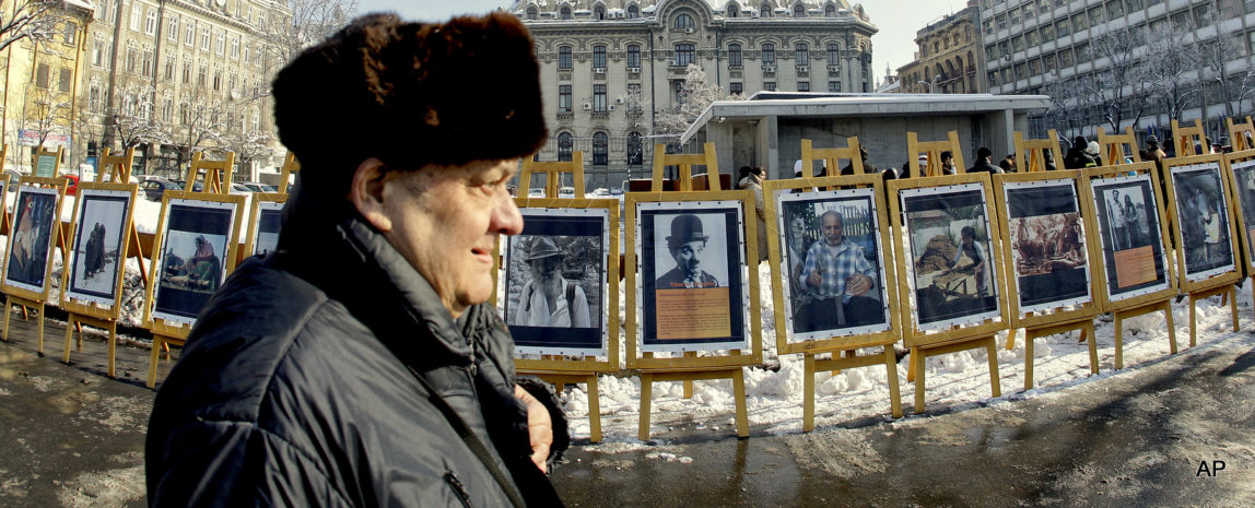An elderly man passes by pictures showing aspects of Romanian Roma community life, and Roma personalities in the world, among them Charlie Chaplin, during an event at the Holocaust Memorial in Bucharest, Romania, Thursday, Jan. 27, 2011. Scores of Romanian Gypsies perished during WWII deportations in the Dniestr region 65 years ago.
