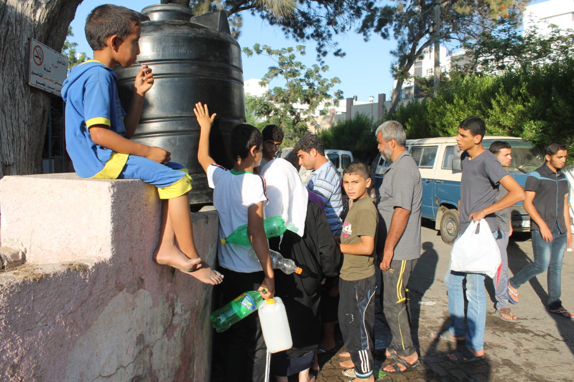 Palestinians displaced by Israeli strikes wait to get water from portable tanks near a makeshift encampment behind Gaza's al-Shifa hospital, Saturday, July 26, 2014. (Joe Catron)