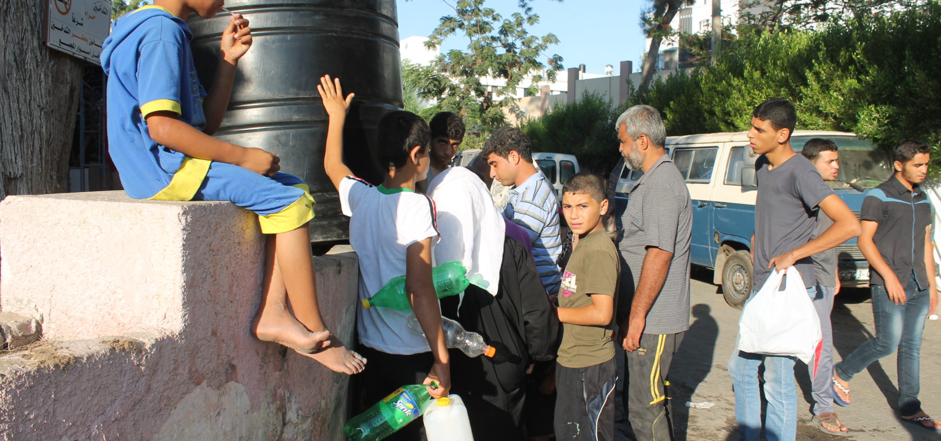 Palestinians displaced by Israeli strikes wait to get water from portable tanks near a makeshift encampment behind Gaza's al-Shifa hospital, Saturday, July 26, 2014. (Joe Catron)