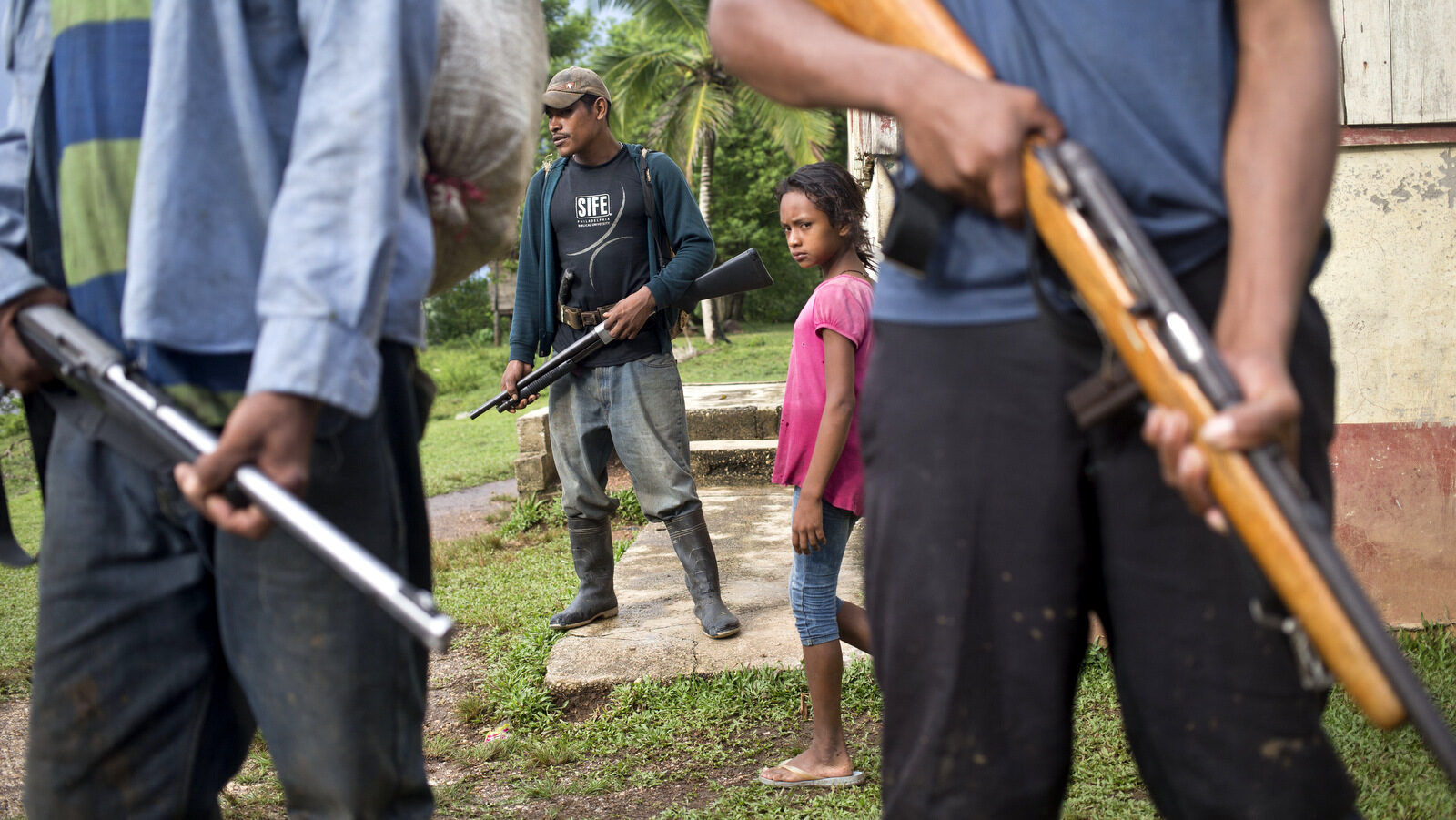 In this Sept. 19, 2015 photo, a Miskito girl walks among Miskito men armed with rifles, which they say they use to defend against attacking colonists, in La Esperanza community, Nicaragua. Miskitos have taken up arms to try to expel the wave of newcomers, who are attracted in part by the area's rich tropical hardwood groves. (AP Photo/Esteban Felix)