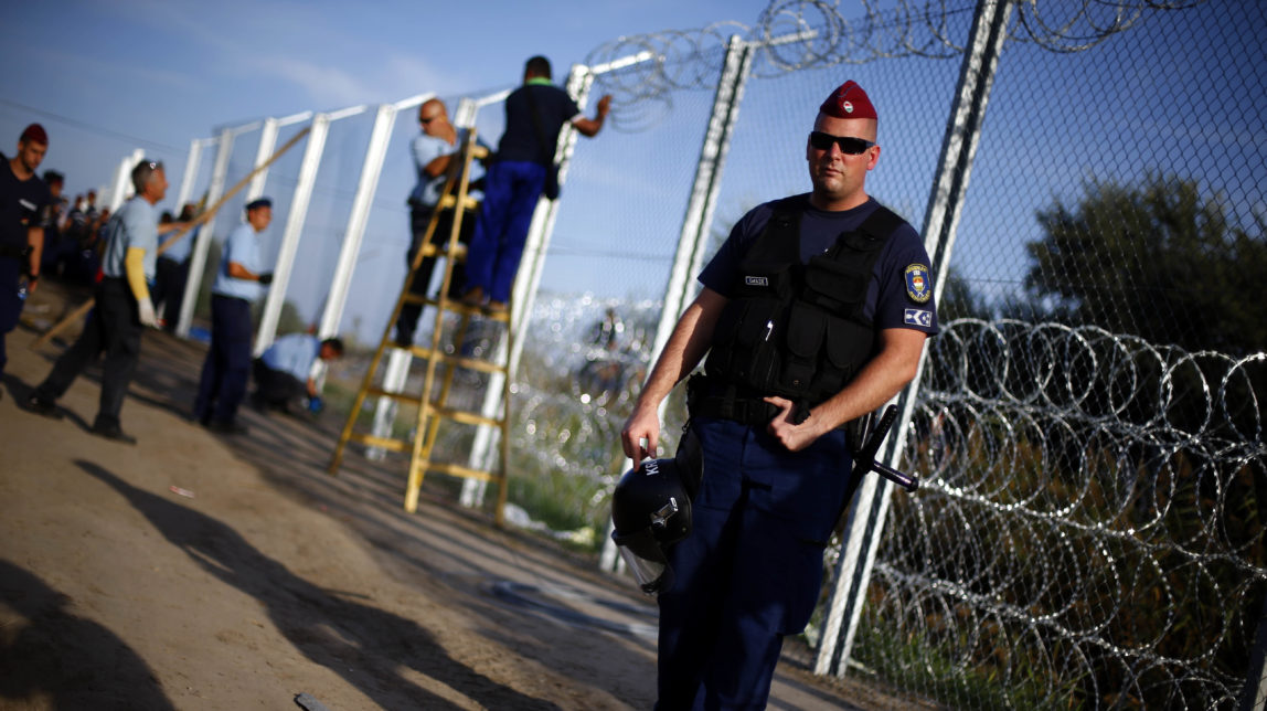 A police officer controls the area as workers begin to erect a fence after Hungarian police officers close the border between Serbia and Hungary in Roszke, southern Hungary, Monday, Sept. 14, 2015.