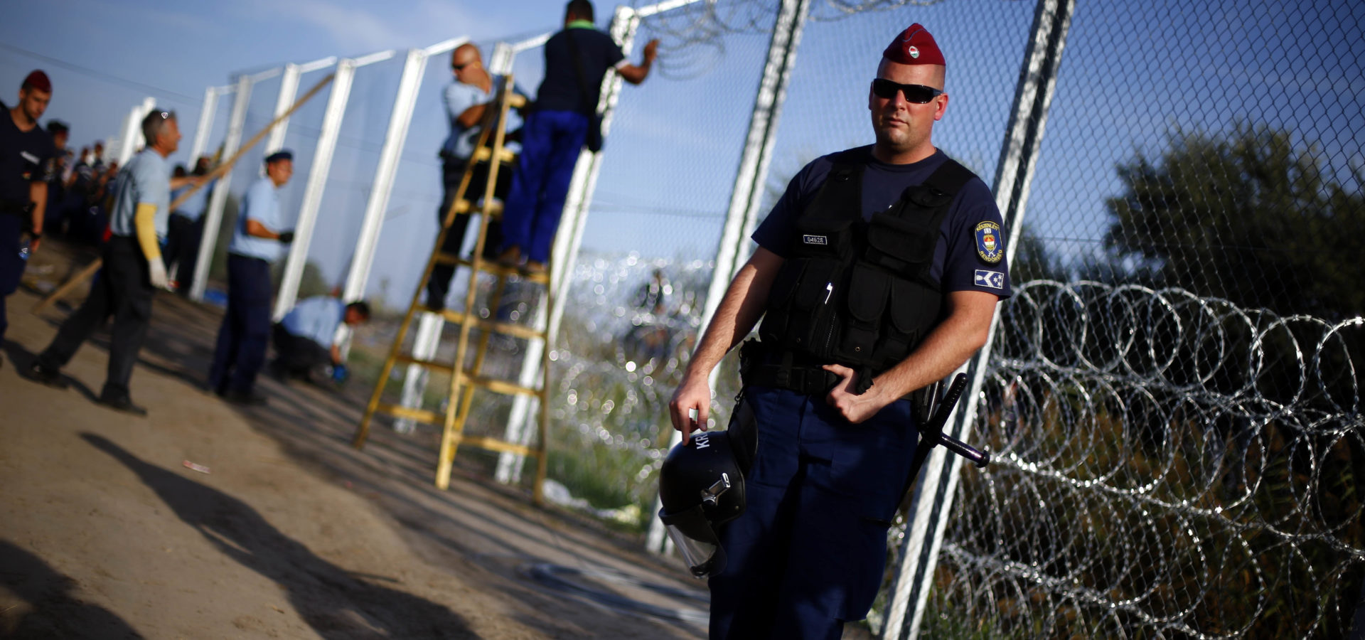 A police officer controls the area as workers begin to erect a fence after Hungarian police officers close the border between Serbia and Hungary in Roszke, southern Hungary, Monday, Sept. 14, 2015.