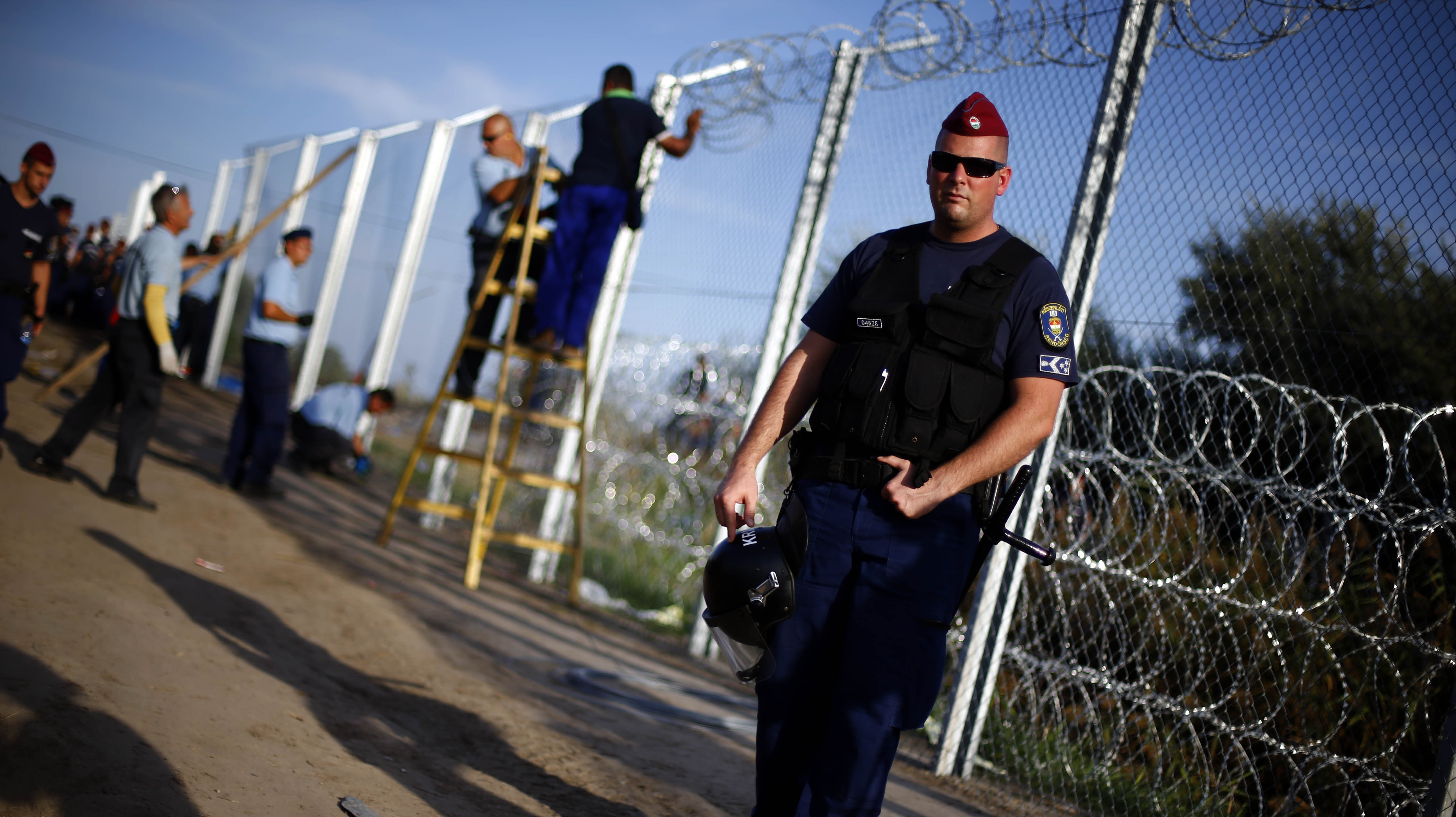 A police officer controls the area as workers begin to erect a fence after Hungarian police officers close the border between Serbia and Hungary in Roszke, southern Hungary, Monday, Sept. 14, 2015. 