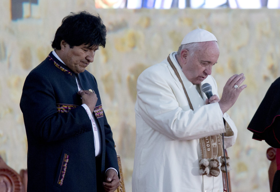 Pope Francis and Bolivia's President Evo Morales pray upon arrival to El Alto International airport in El Alto, Bolivia, Wednesday, July 8, 2015. The pouch Francis is wearing around his neck was given to him by Morales. It's woven of alpaca with indigenous trimmings and traditionally used by people in the Andes to hold coca leaves, which they chew to ward off the ill effects of extreme altitude. (AP Photo/Eduardo Verdugo)