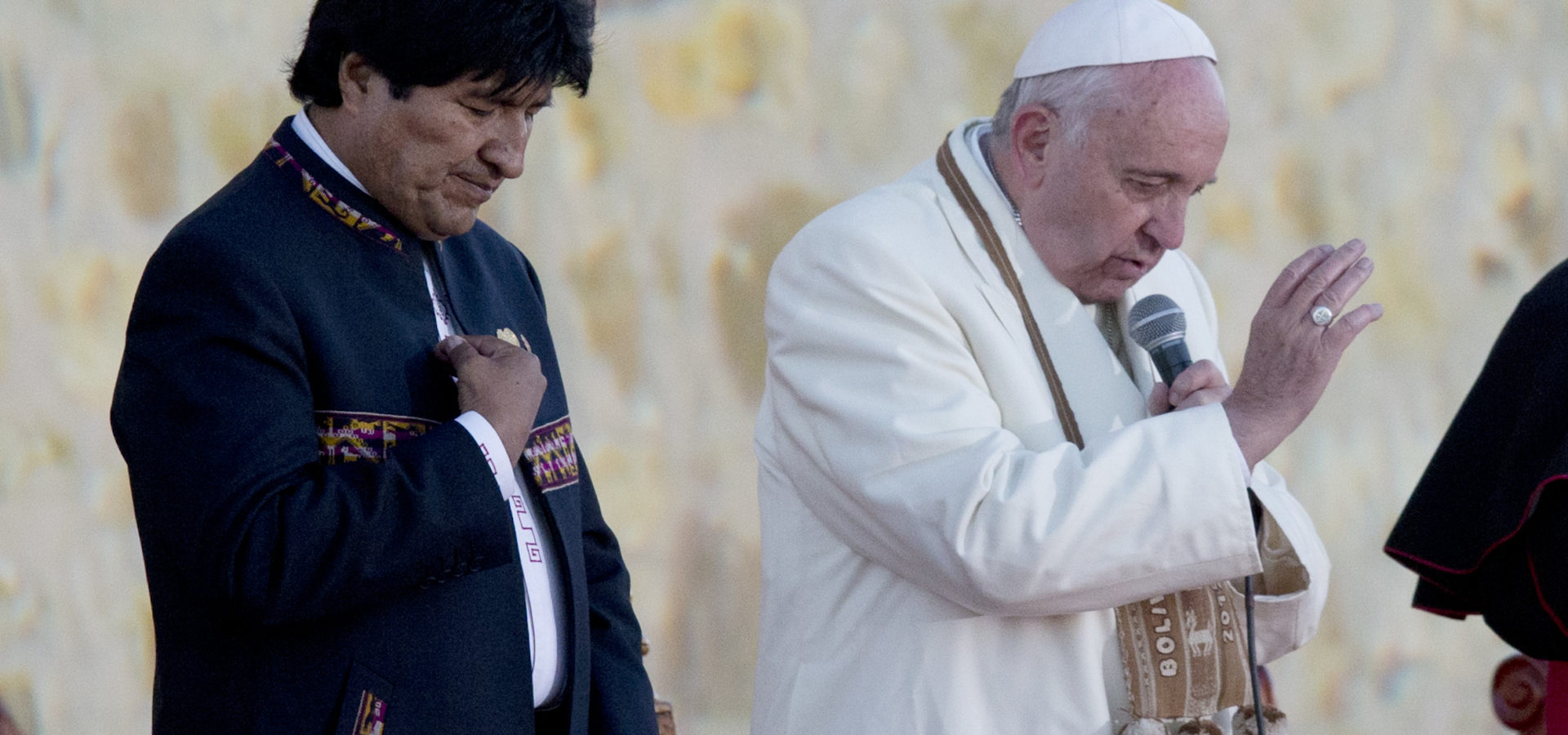 Pope Francis and Bolivia's President Evo Morales pray upon arrival to El Alto International airport in El Alto, Bolivia, Wednesday, July 8, 2015. The pouch Francis is wearing around his neck was given to him by Morales. It's woven of alpaca with indigenous trimmings and traditionally used by people in the Andes to hold coca leaves, which they chew to ward off the ill effects of extreme altitude. (AP Photo/Eduardo Verdugo)