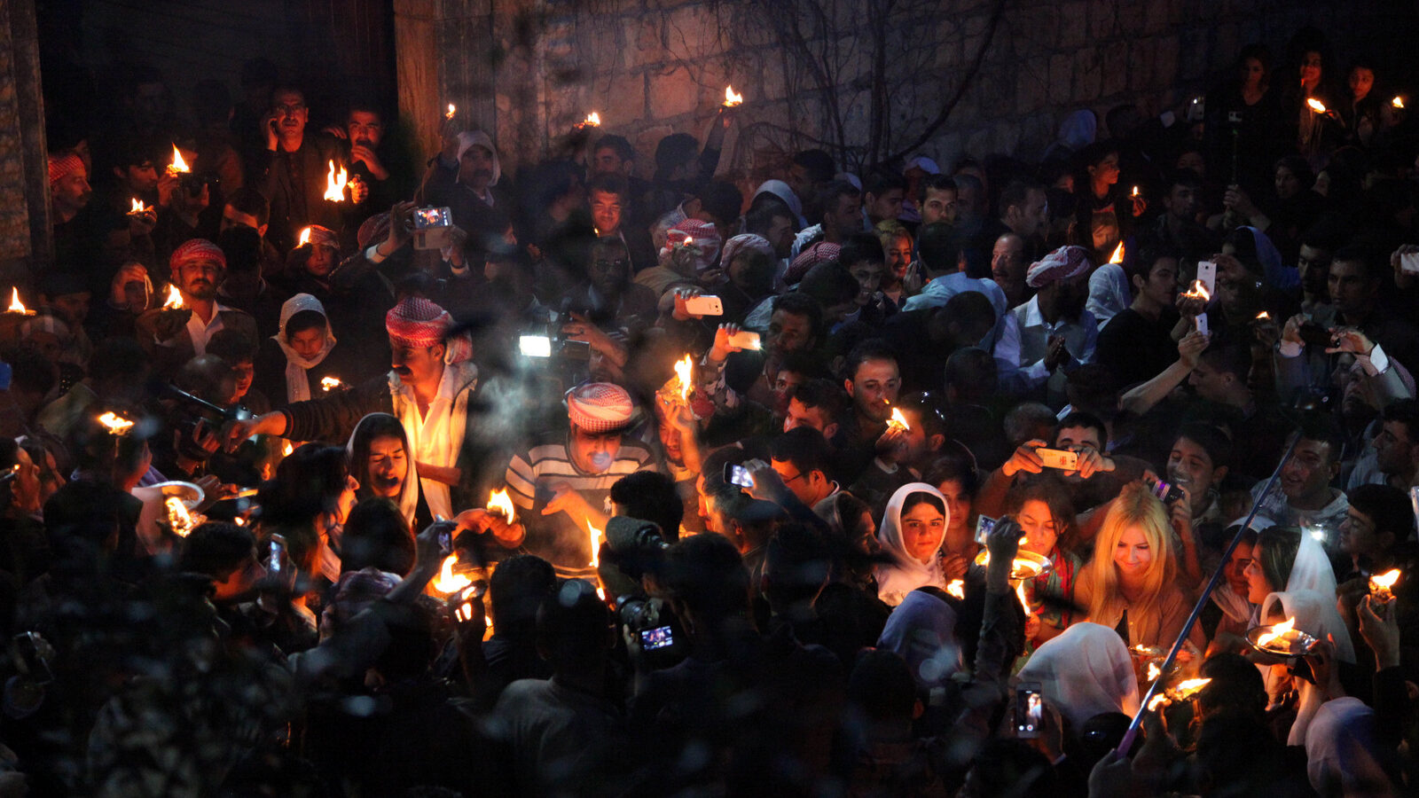 In this Tuesday, April 15, 2015 photo, Yazidis gather to light flames, some capturing the scene with their mobile phones, at the holy shrine of Lalish, 57 kilometers (35 miles) north of militant-held Mosul, Iraq, as thousands celebrate the New Year, their first since Islamic State militants swept through the area last summer. Yazidis, a centuries-old religion derived from Zoroastrianism, Christianity and Islam, believe that the occasion marks the creation of the earth, also the day that God created the holy shrine in Lalish. (AP Photo/Seivan M.Salim)