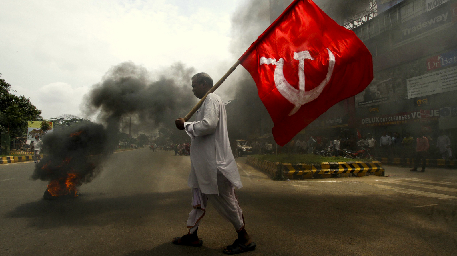 An activist of the Indian trade union group holds a party flag as he walks past a burning tyre set up as a road blockade during a daylong nationwide strike in the eastern Indian city Bhubaneswar, India, Wednesday, Sept. 2, 2015. Normal life was affected in several parts of the state following a day-long nationwide general strike called by ten central trade unions to protest changes in labour laws and privatisation of Public Sector Undertaking’s (PSU) by the ruling Bharatiya Janata Party (BJP) government. (AP Photo/Biswaranjan Rout)