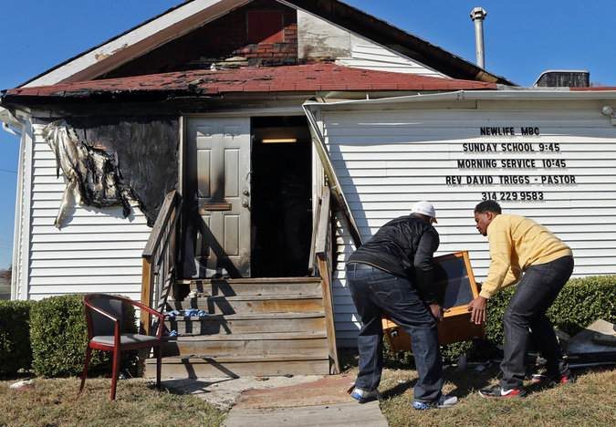 In this Sunday, Oct. 18, 2015 photo, Deacon Clinton McMiller, left, and Pastor David Triggs carry a cabinet back into the church after an outdoor service due to a fire at the New Life Missionary Baptist Church in St. Louis. Someone has been setting fire to predominantly black churches in the St. Louis area, and investigators are trying to determine if the arsonist is targeting either religion or race. (J.B. Forbes/St. Louis Post-Dispatch via AP)