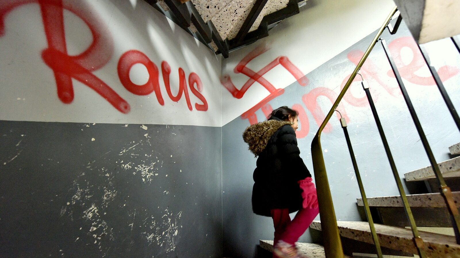 A refugee child walks on the stairway in a refugee housing in Waltrop, western Germany, painted with a swastika graffiti and a writing "get out dogs", Tuesday, Oct. 13, 2015. Unknown persons sprayed extremist anti refugee graffities on and in several refugee homes in the city the night before. (AP Photo/Martin Meissner)