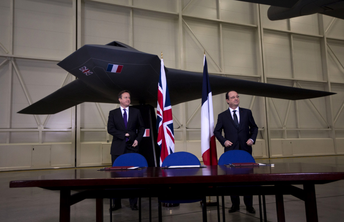 British Prime Minister David Cameron, left, and French President Francois Hollande stand backdropped by a model of a concept design for a future unmanned combat air vehicle as they wait for memorandums of understandings and an agreement to be signed before the start of their press conference at their one-day summit at the RAF Brize Norton air base in Brize Norton, England, Friday, Jan. 31, 2014. The one-day summit covered military cooperation, including talks over armed drones, anti-ship missiles, and underwater mine detectors, as well as a joint Franco-British force of 10,000 soldiers due to be formed in the next few years. (AP Photo/Matt Dunham)