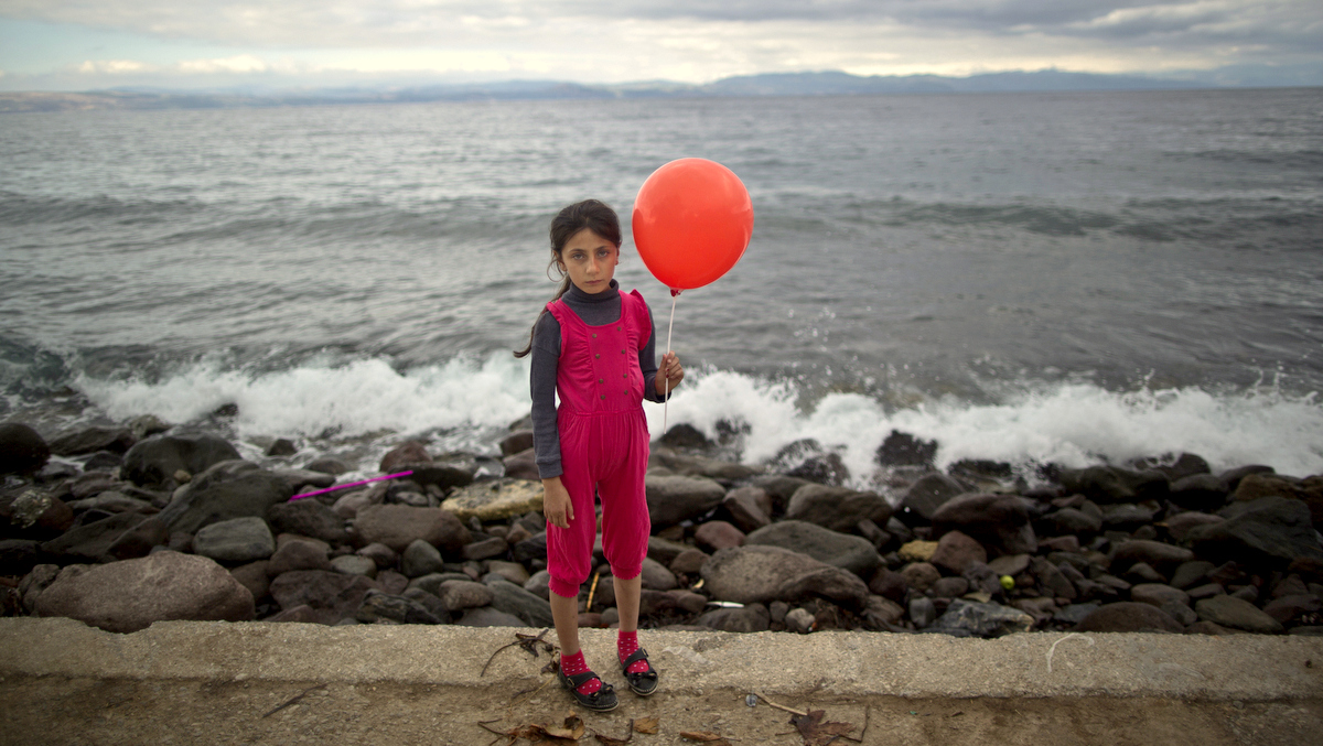 In this photo taken on Friday, Oct. 2, 2015, Syrian refugee Raghad Faleh, 8, who came with her family from Idlib, Syria, poses for a picture while holding a balloon given to her by volunteers, a few hours after she and her family arrived on a dinghy from the Turkish coast to the northeastern Greek island of Lesbos. “My feet are killing me from pain, I walked a lot,” Faleh said. (AP Photo/Muhammed Muheisen)