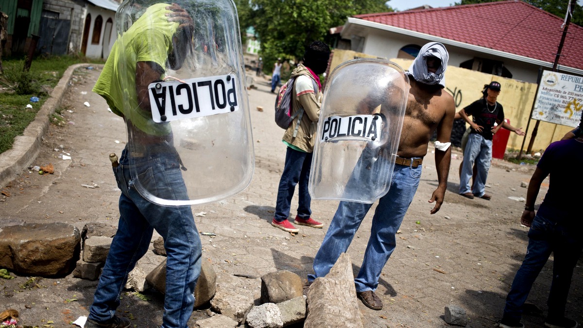 Masked miners and their family members, some holding police shields, patrol a road block they set up in their neighborhood in El Limon, Nicaragua, Wednesday, Oct. 7, 2015. Clashes between police and miners erupted Tuesday when police tried to remove roadblocks set up all over town by miners who went on strike two weeks ago to protest the firing of several of their union members by the Canadian mine company B2Gold. According to police, one officer died in the violence. (AP Photo/Esteban Felix)