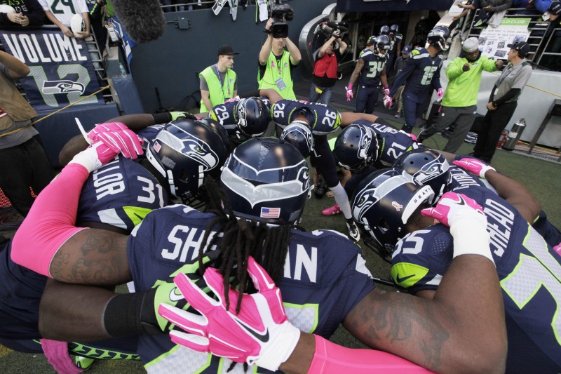 Seattle Seahawks strong safety Kam Chancellor, left, Richard Sherman, center, and DeShawn Shead, right, huddle with the rest of the Seattle Seahawks "Legion of Boom" defensive players before an NFL football game against the Detroit Lions, Monday, Oct. 5, 2015, in Seattle. Both teams are wearing pink items for breast cancer awareness during the game. (AP Photo/Elaine Thompson)